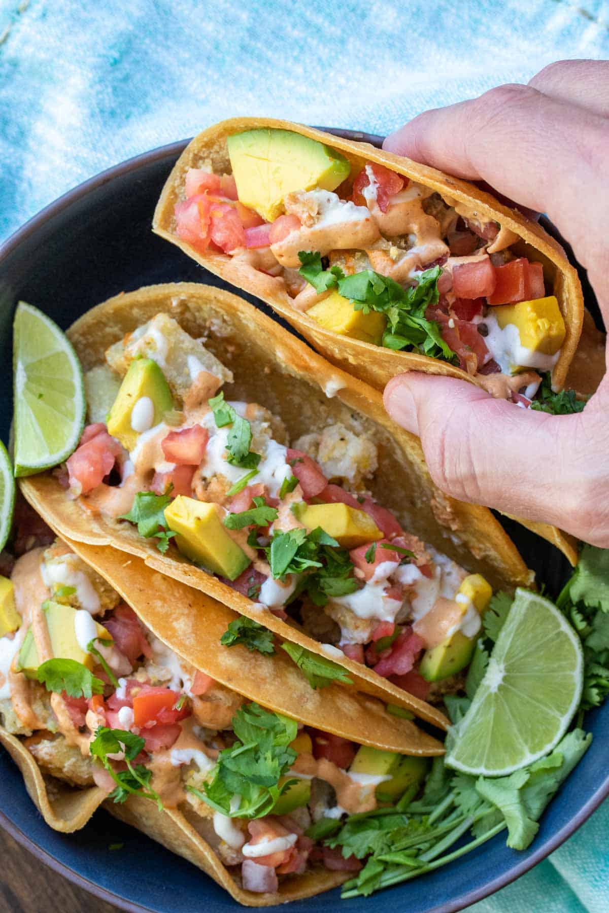 Hand taking a potato tacos from a bowl of them