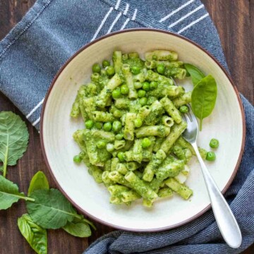 White bowl filled with pasta coated with kale pesto and mixed with peas