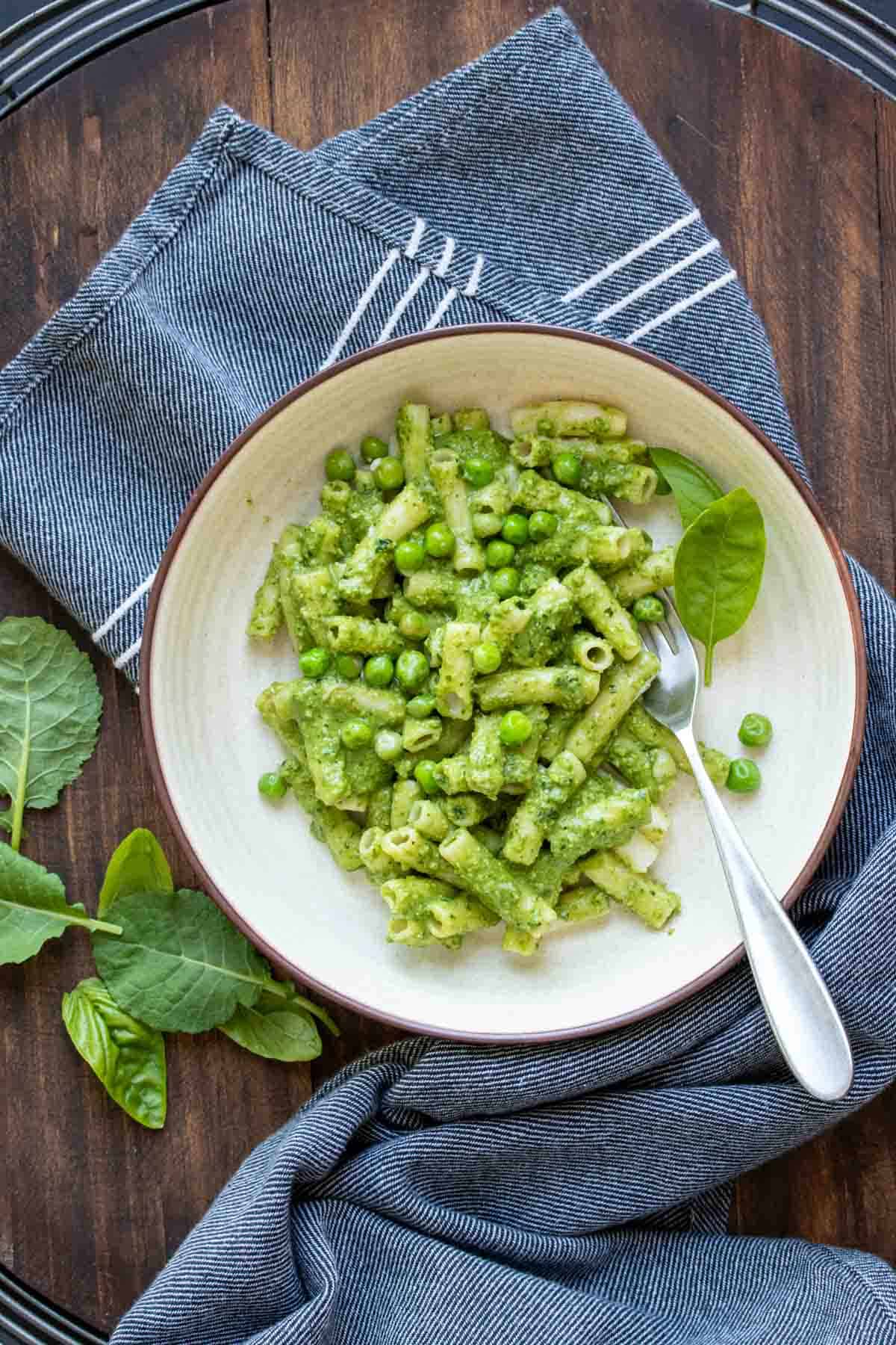 White bowl filled with pasta coated with kale pesto and mixed with peas