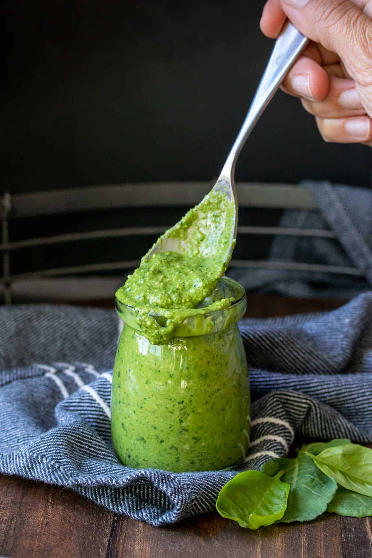 Spoon coming out of a glass jar with pesto inside