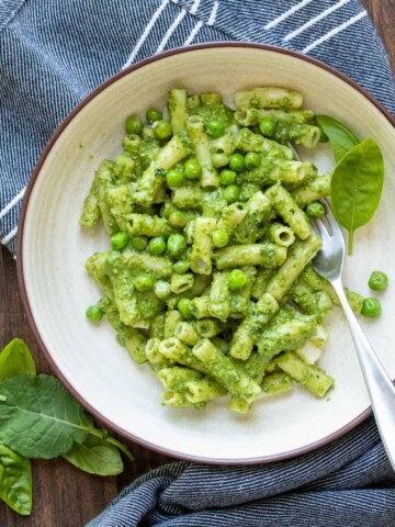 Fork in a bowl of pasta and peas mixed with kale pesto