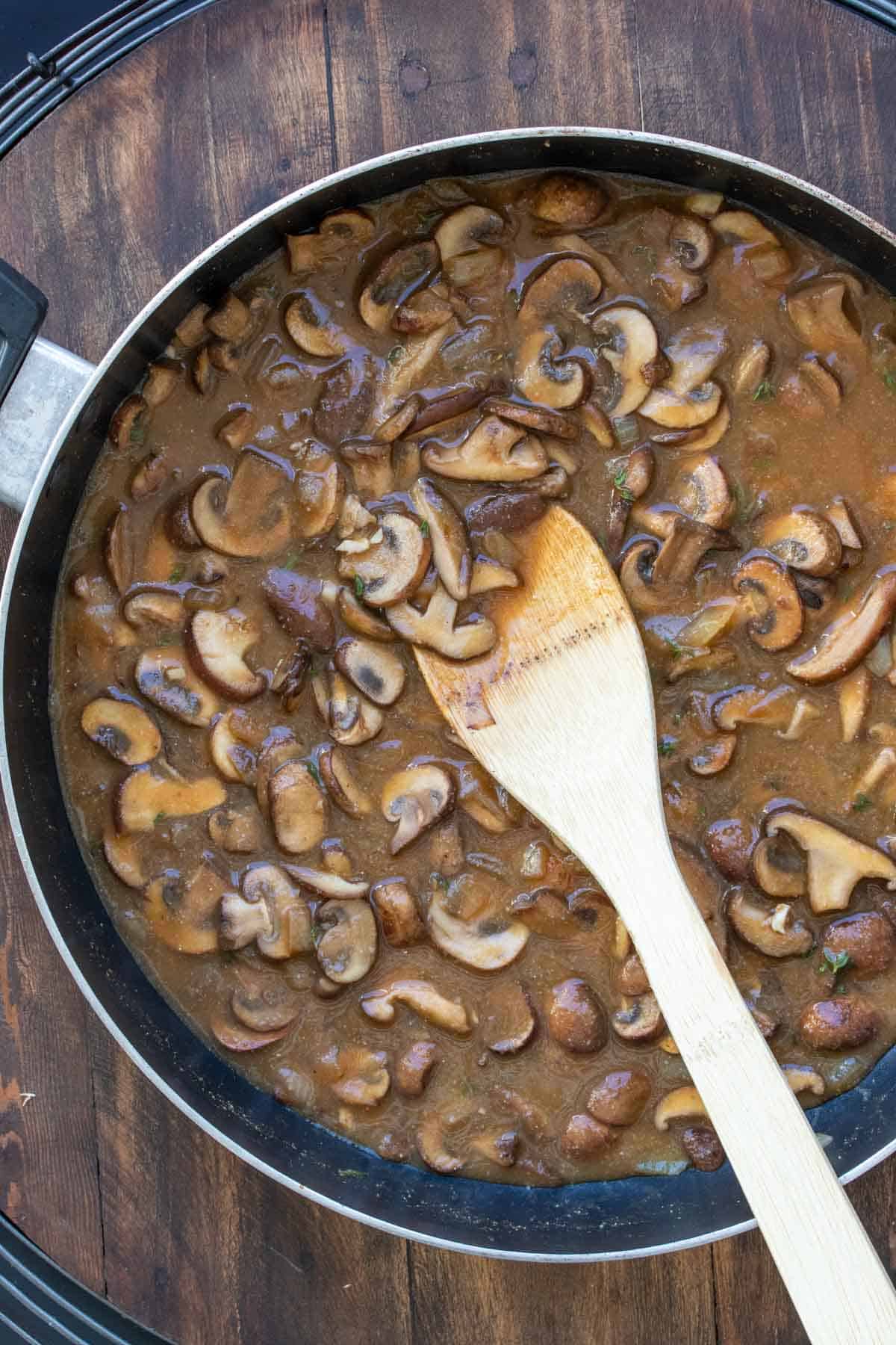 Mushrooms cooking in a brown colored broth in a pan.