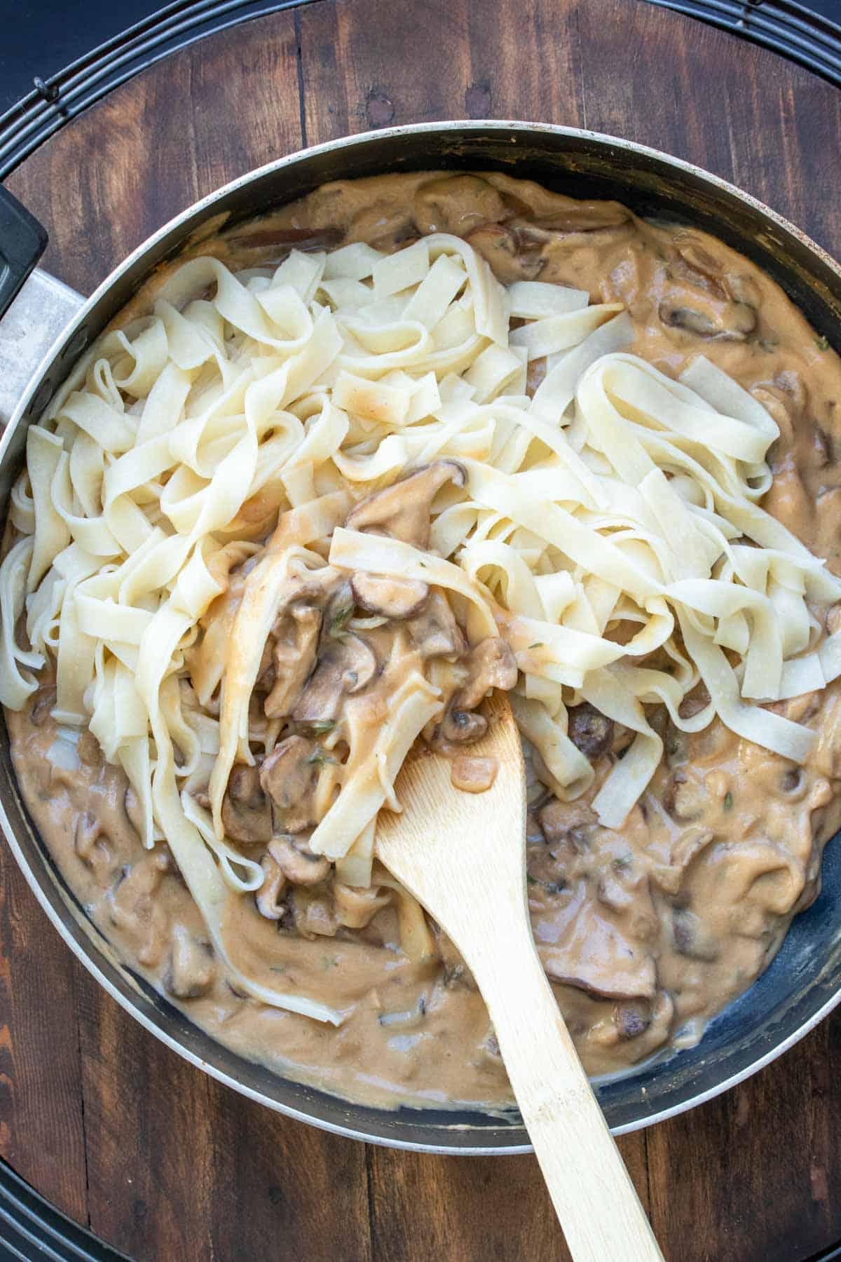 Fettuccini noodles bring mixed into a tan creamy sauce with mushrooms.