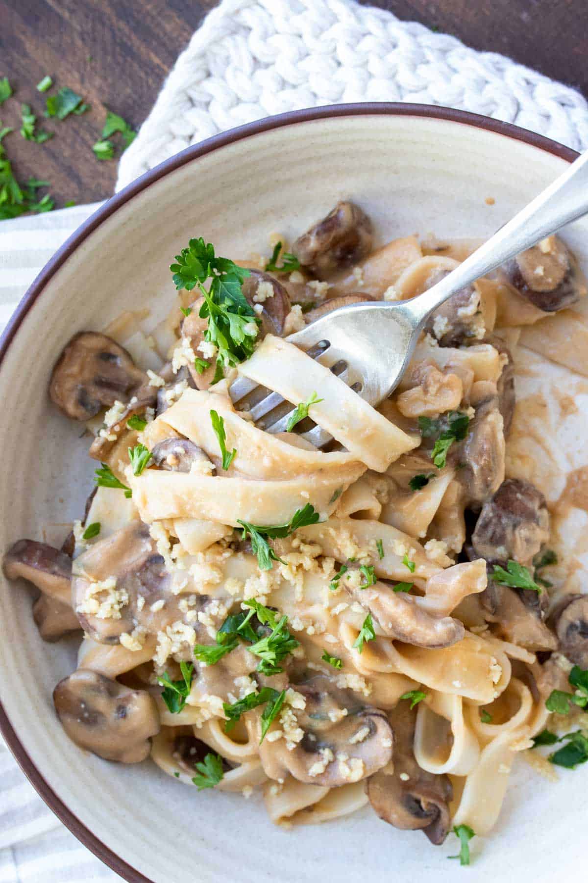 Fork getting a bite from a bowl of creamy mushroom stroganoff in a white bowl.