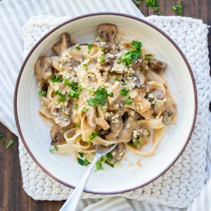 White bowl filled with mushroom stroganoff and topped with chopped parley.