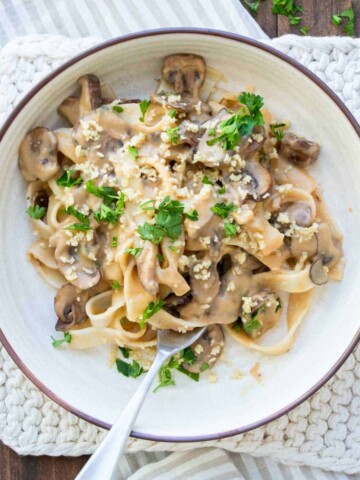 White bowl filled with mushroom stroganoff and topped with chopped parley.