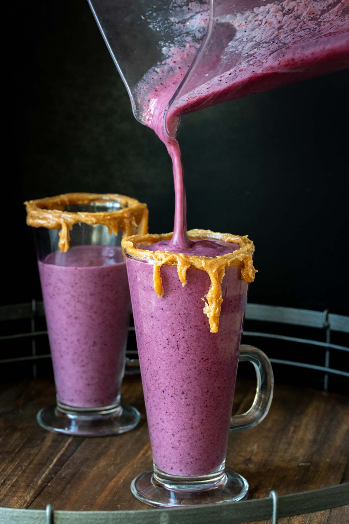 Container pouring a PB&J smoothie into a glass with peanut butter on the rim