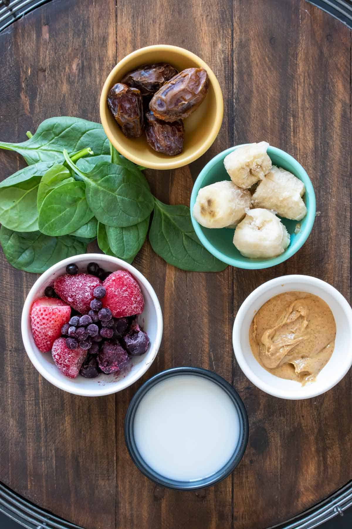 Bowls with ingredients to make a PB&J smoothie with greens