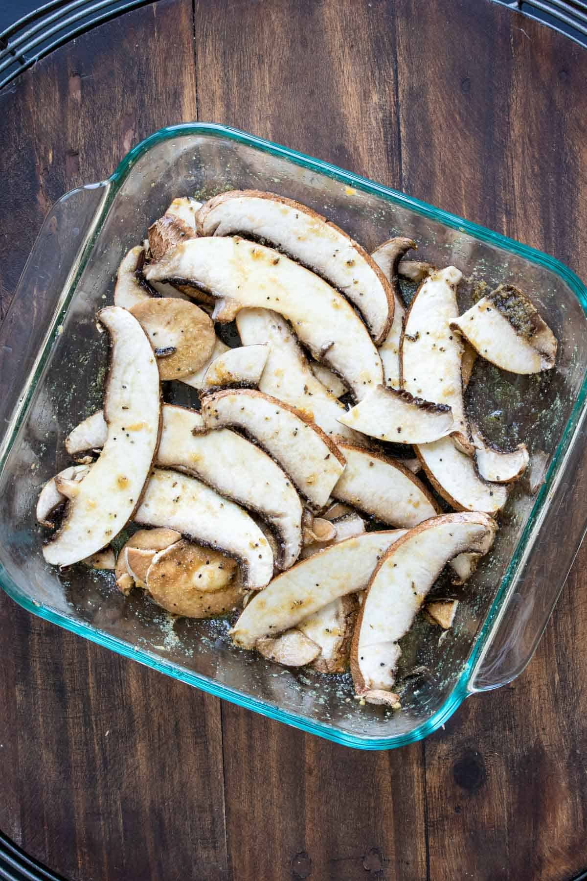 Slices of portobello mushroom topped with spices in a glass baking dish