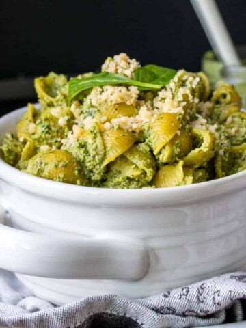 Pasta and pesto filling a white bowl on a grey towel