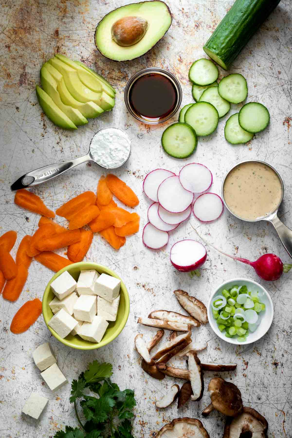 A variety of vegetables and toppings to make a homemade sushi bowl laying on a white surface with brown specks