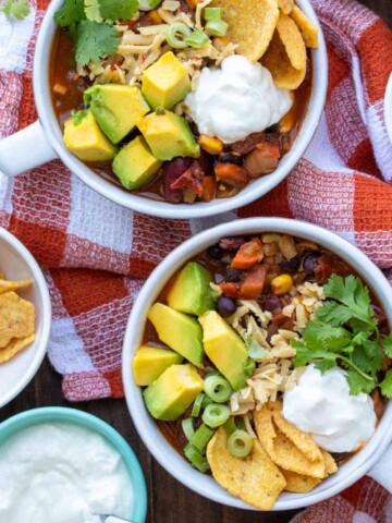 Two white bowls filled with vegetable chili topped with lots of toppings