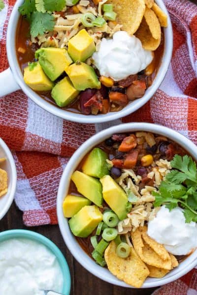 Two white bowls filled with vegetable chili topped with lots of toppings