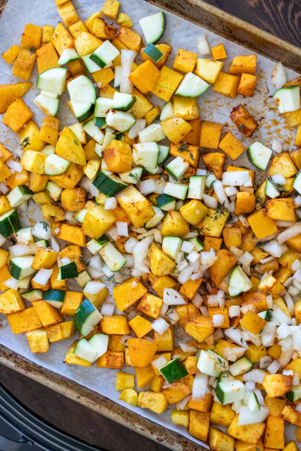 Cut pieces of zucchini and butternut squash on a baking sheet with spices