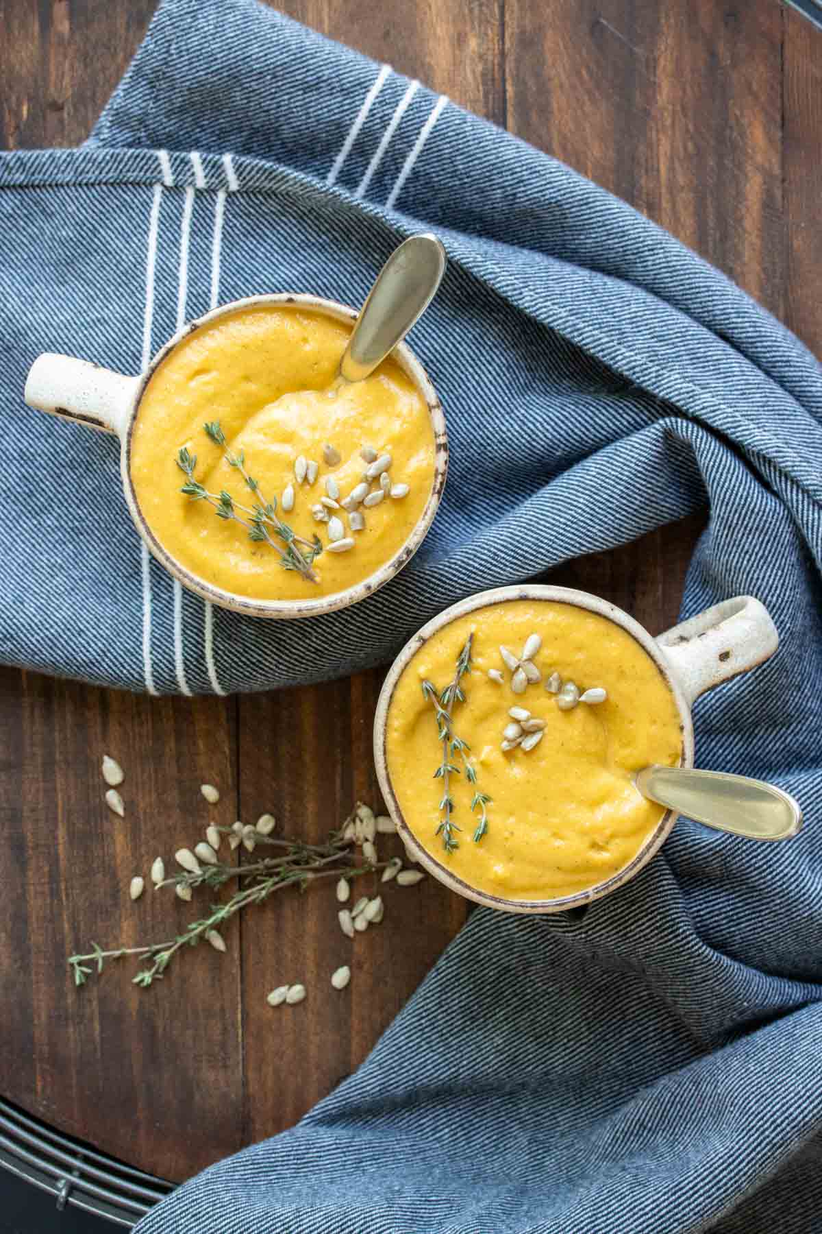 Two mugs with pureed winter squash soup and spoons in them