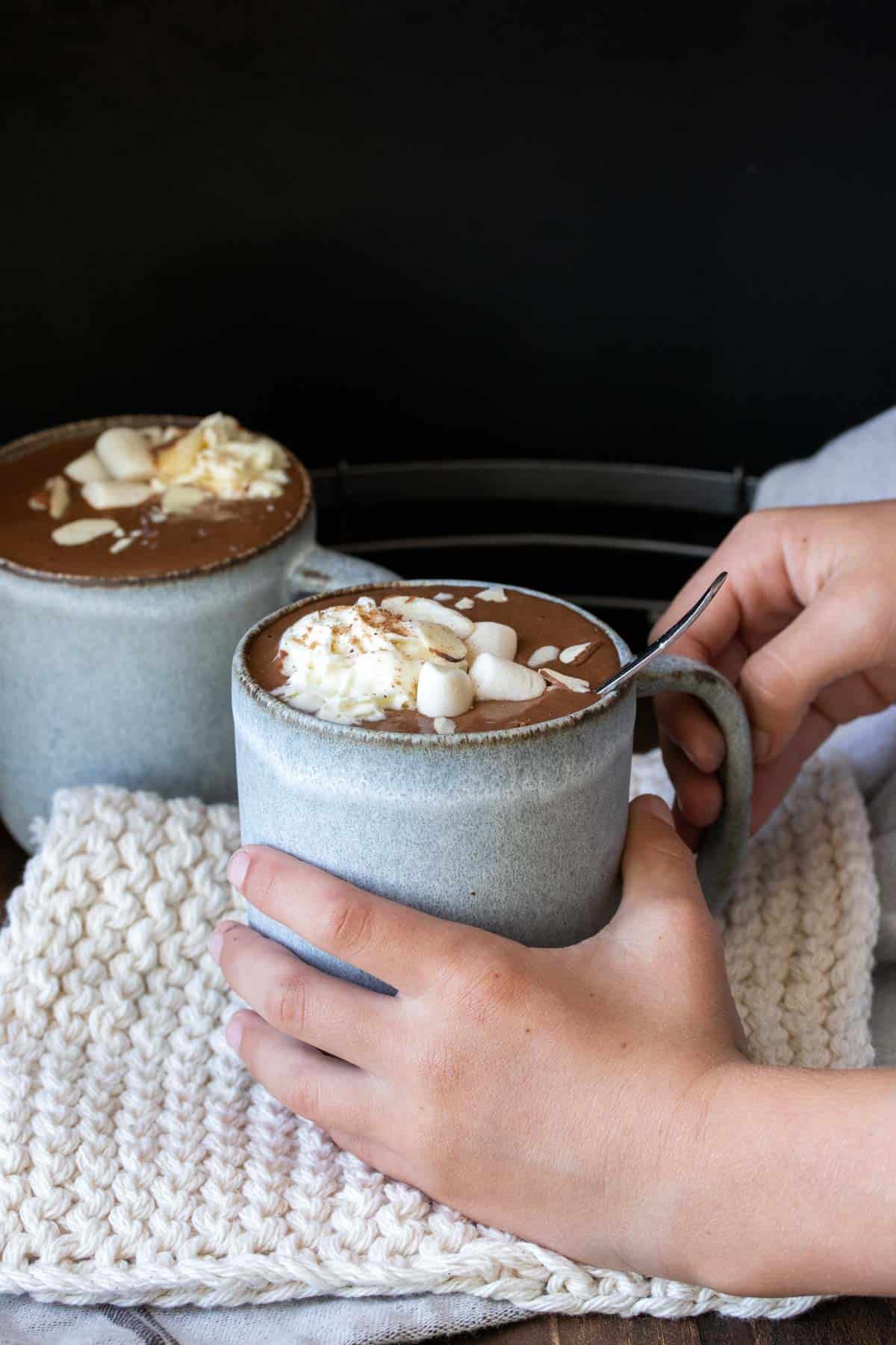 Hands grabbing a grey mug filled with hot cocoa