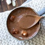 Spoon getting a taste of hot cocoa with marshmallows from a grey mug