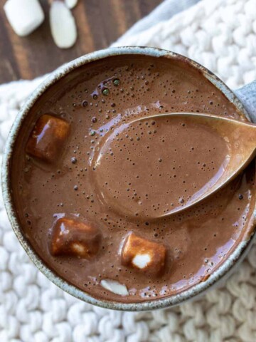 Spoon getting a taste of hot cocoa with marshmallows from a grey mug