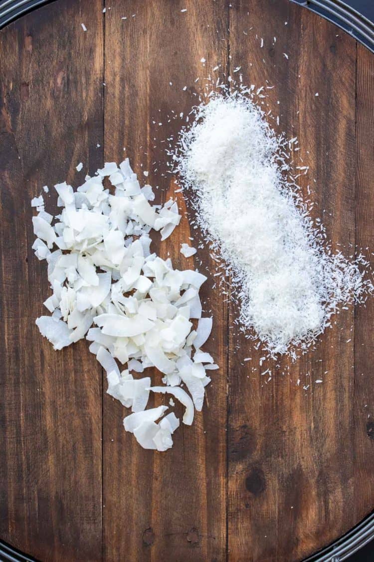 A pile of shredded coconut next to a pile of flaked coconut on a wooden surface