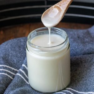 Wooden spoon dripping coconut butter into a glass jar.