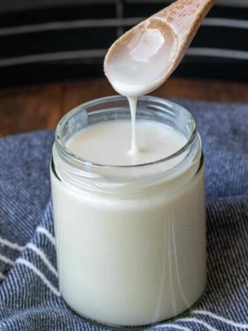 Wooden spoon dripping coconut butter into a glass jar.