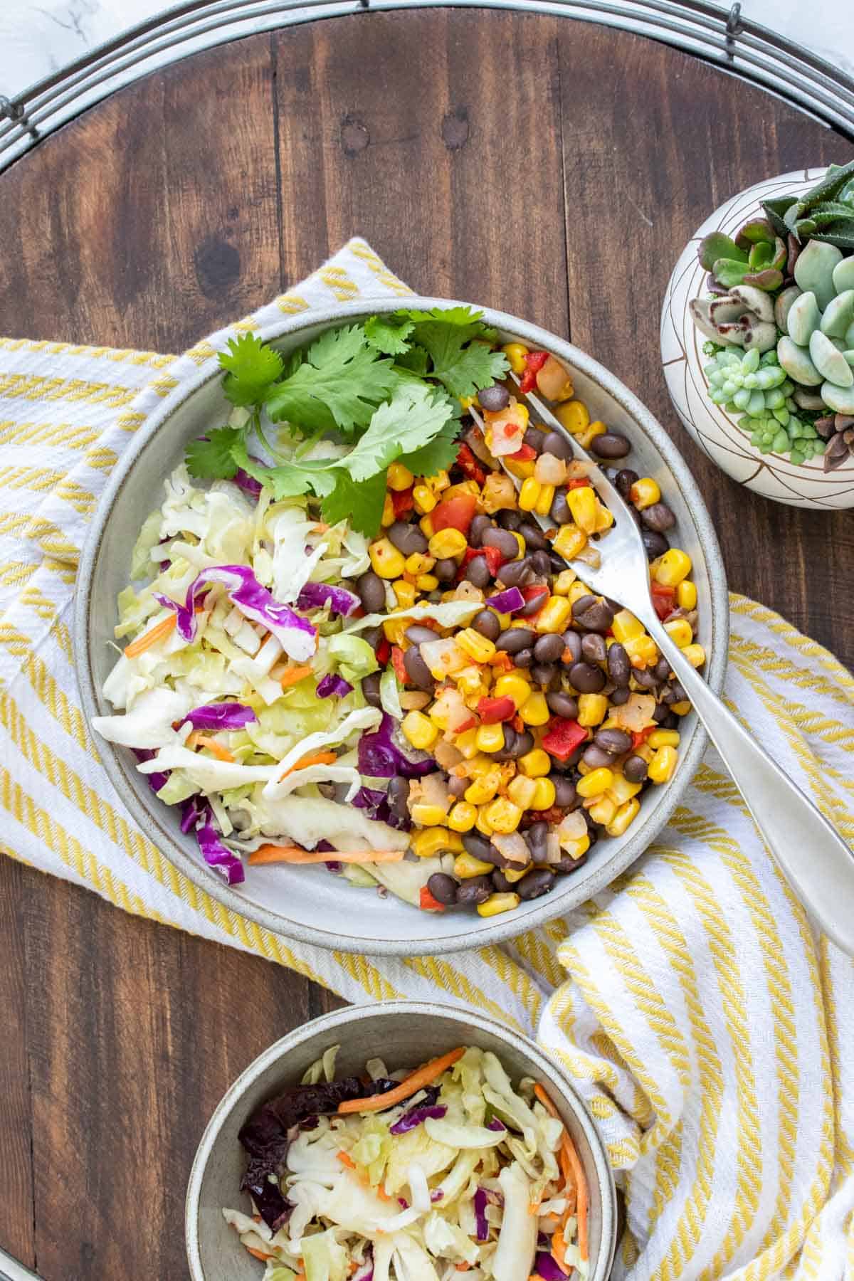 Plate with a corn and bean mix next to cabbage salad