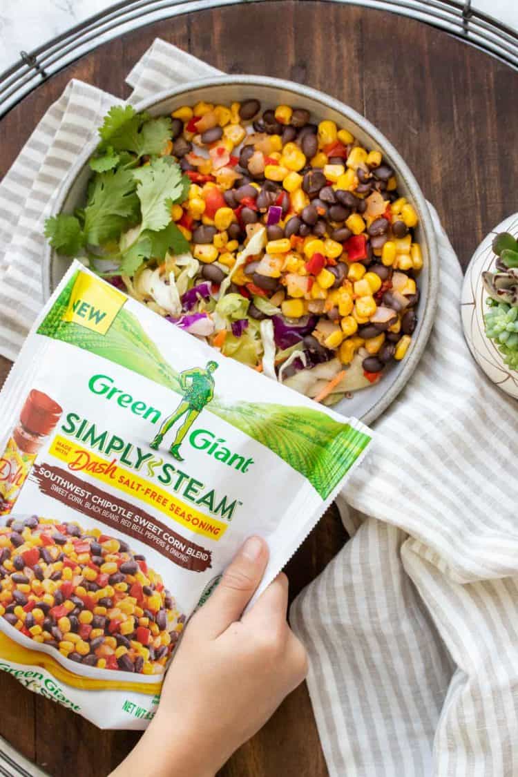 Hands holding a bag of frozen veggies over a plate of food