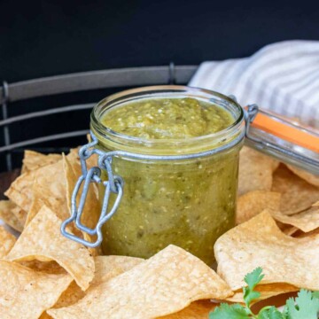 Glass jar with salsa verde sitting on a platter filled with chips