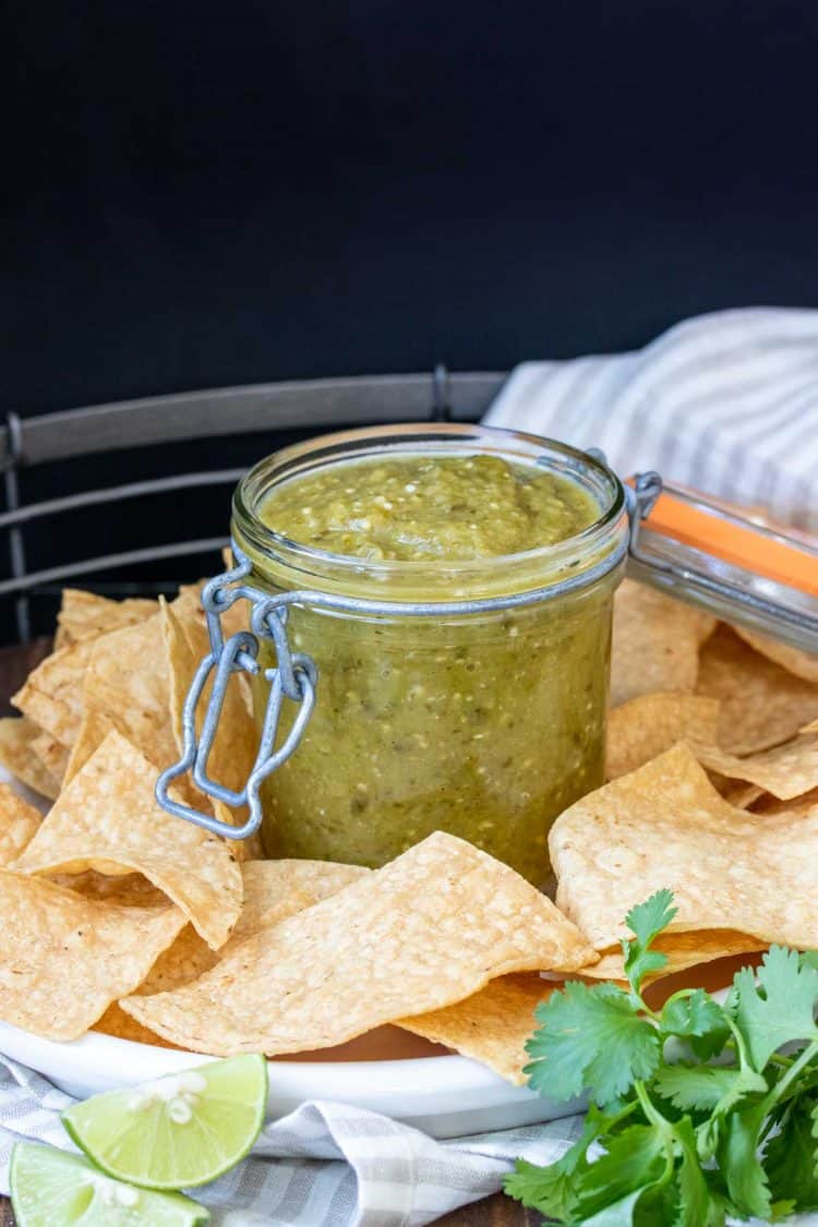 Glass jar with salsa verde sitting on a platter filled with chips