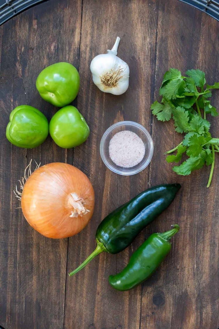 Ingredients needed to make tomatillo salsa laid out on a wooden surface