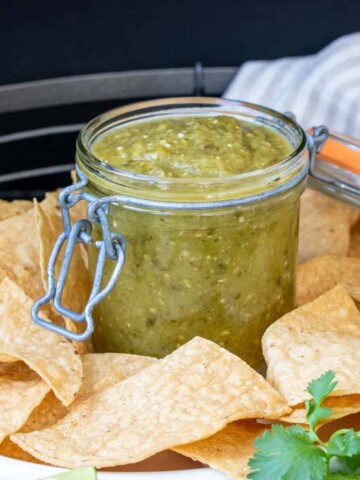 Glass jar filled with tomatillo salsa and surrounded by chips