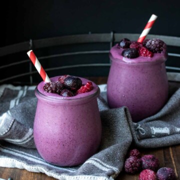 Two glass jars filled with a purple banana berry smoothie and topped with berries