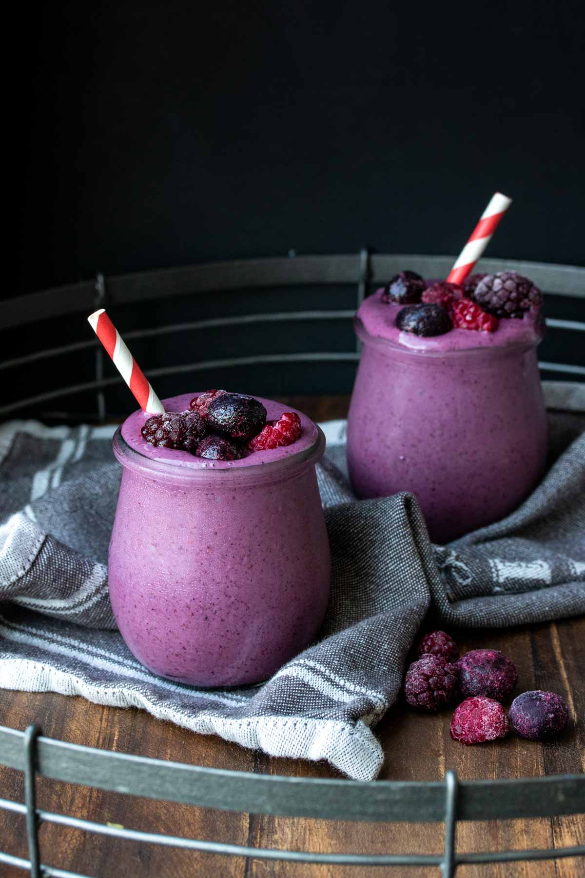 Two glass jars filled with a purple banana berry smoothie and topped with berries