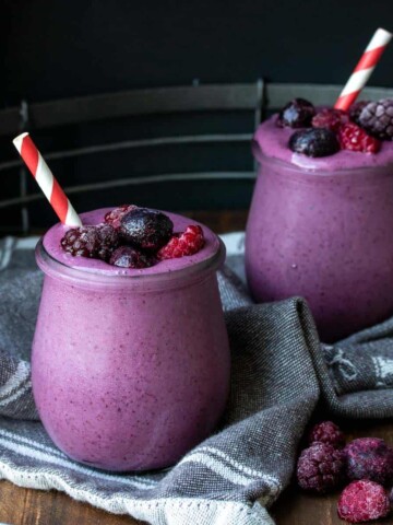 Two glass jars with purple smoothies next to berries