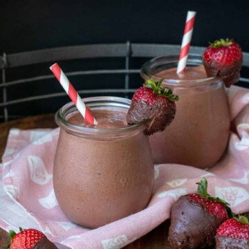 Two glass jars filled with a chocolate strawberry smoothie and strawberries on the side