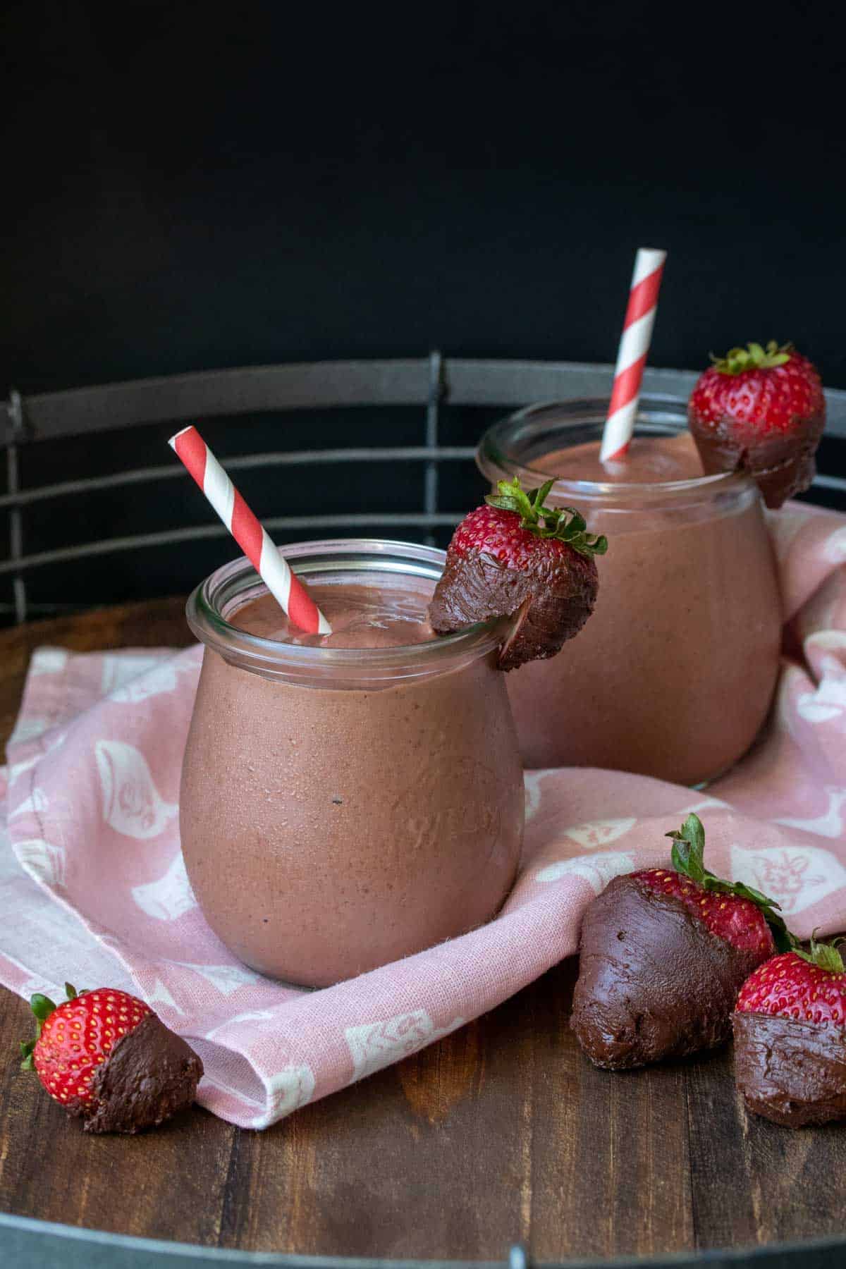 Two glass jars filled with a chocolate strawberry smoothie and strawberries on the side