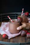 Hand grabbing a jar of chocolate strawberry smoothie from a wooden tray