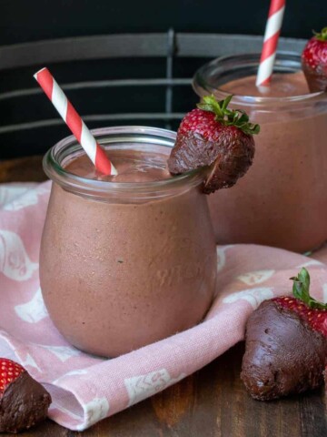 Two glass jars with chocolate covered strawberry smoothies and surrounded by strawberries with chocolate