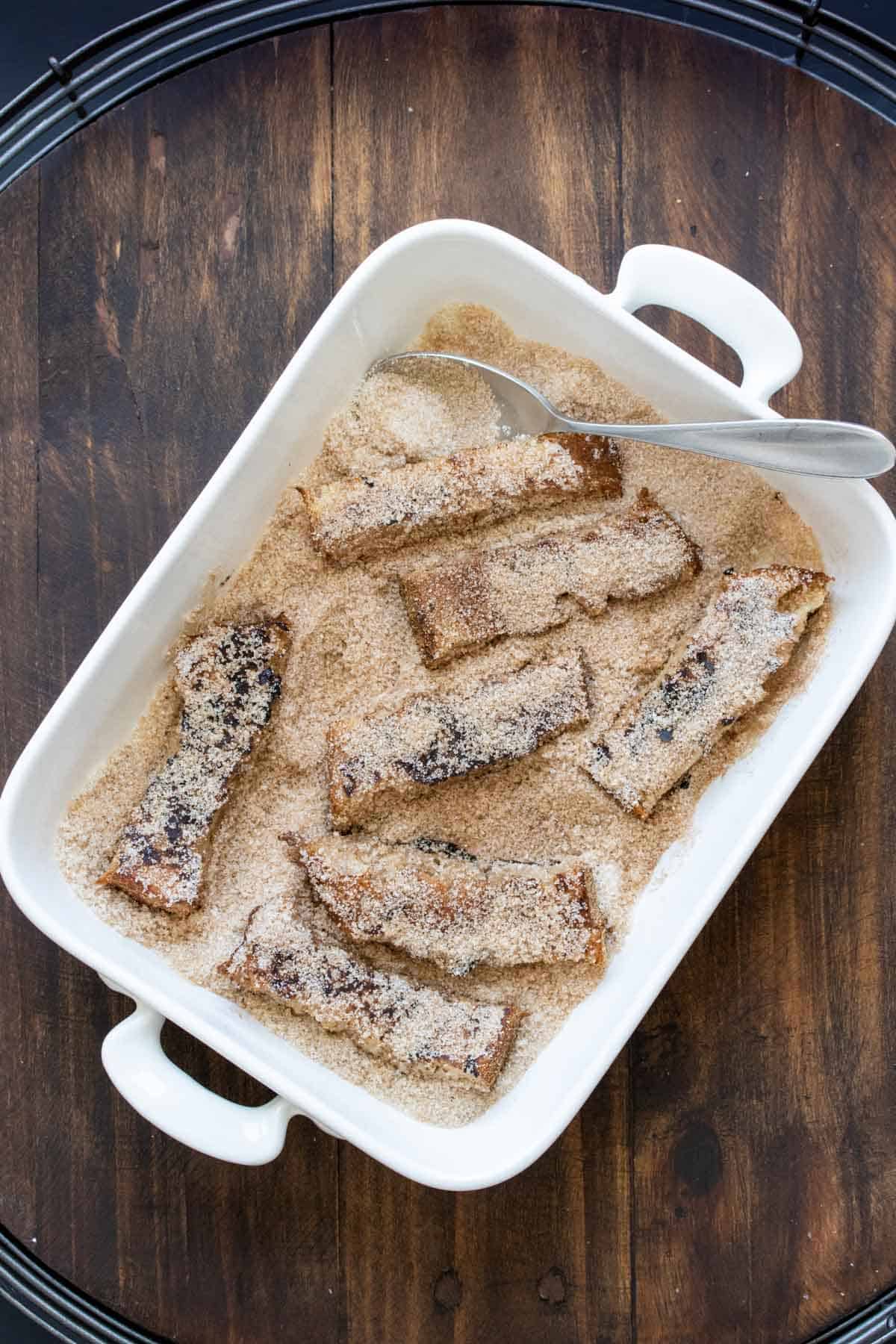 Cooked french toast sticks getting coated in a pan of cinnamon sugar