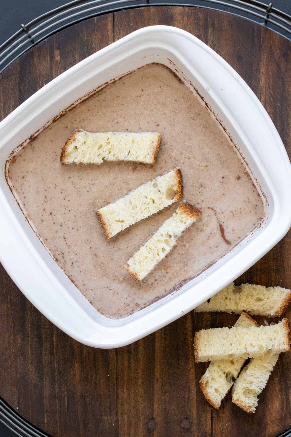 White baking dish with tan liquid and strips of bread soaking in