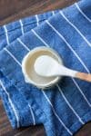 Top view of a wooden spoon getting a bite of creamy aioli from a jar