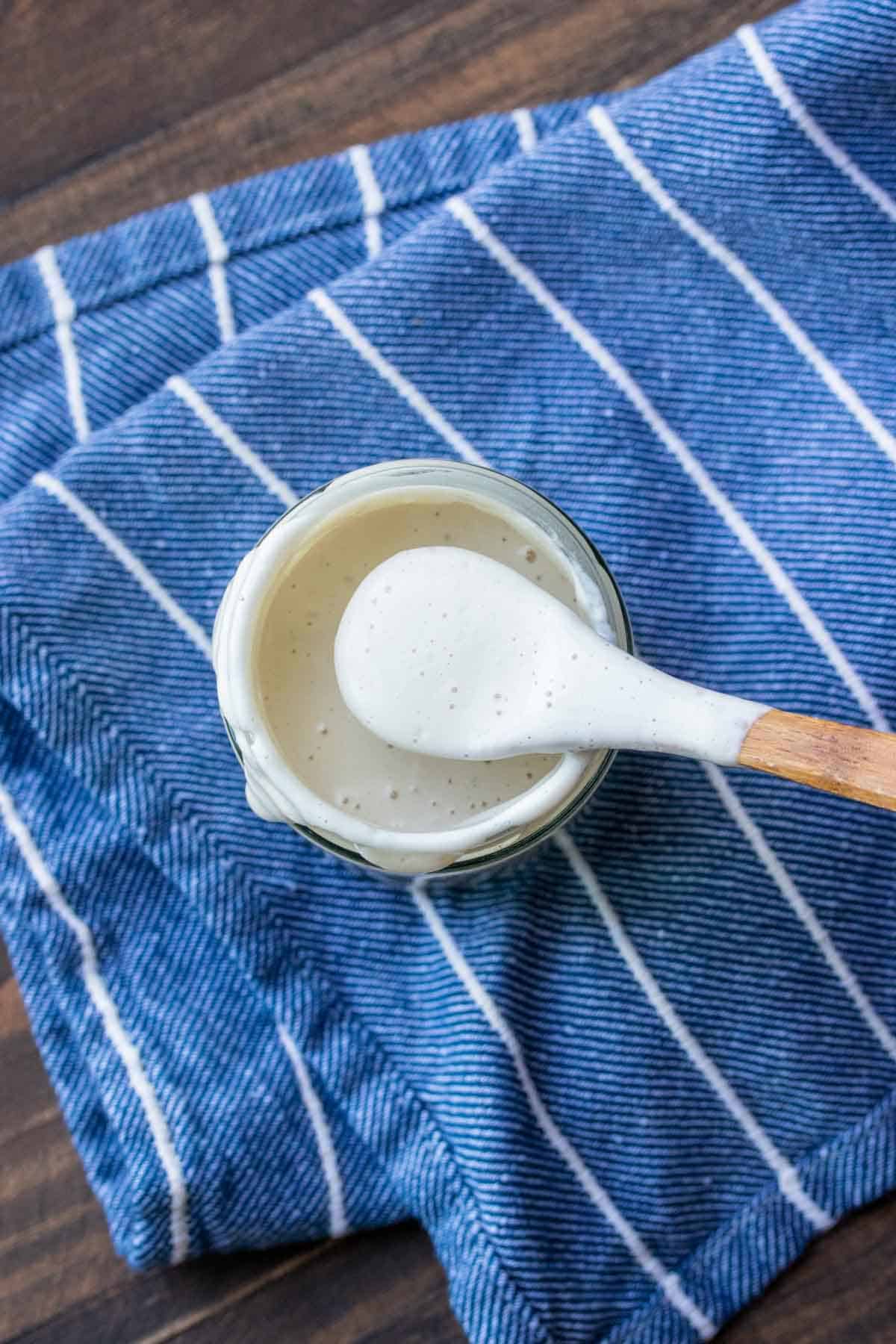 Top view of a wooden spoon getting a bite of creamy aioli from a jar