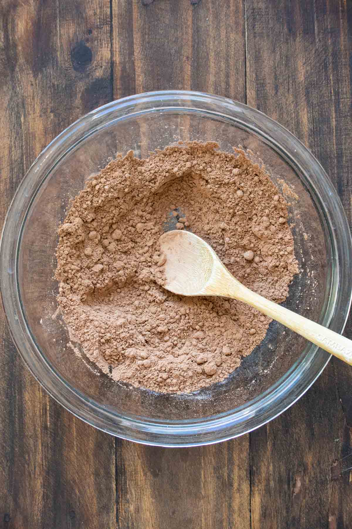 Wooden spoon mixing cocoa powder and sugar in a glass bowl.
