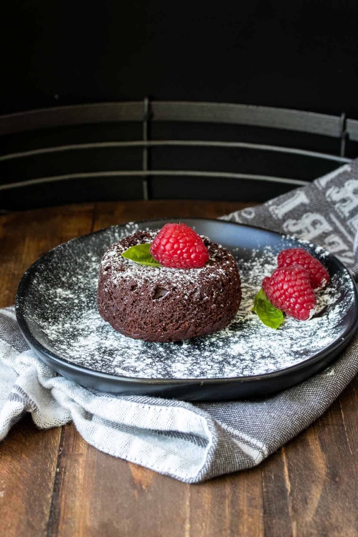 A mini chocolate cake dusted with powdered sugar on a black plate.