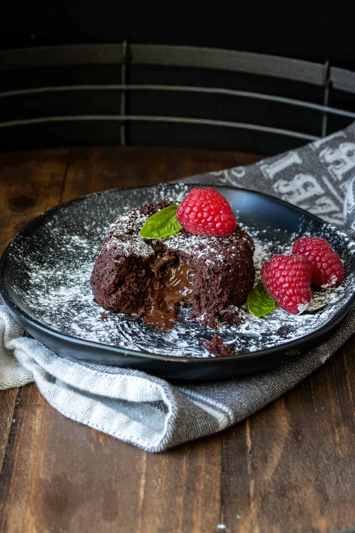 Cut open chocolate lava cake on a black plate with raspberries