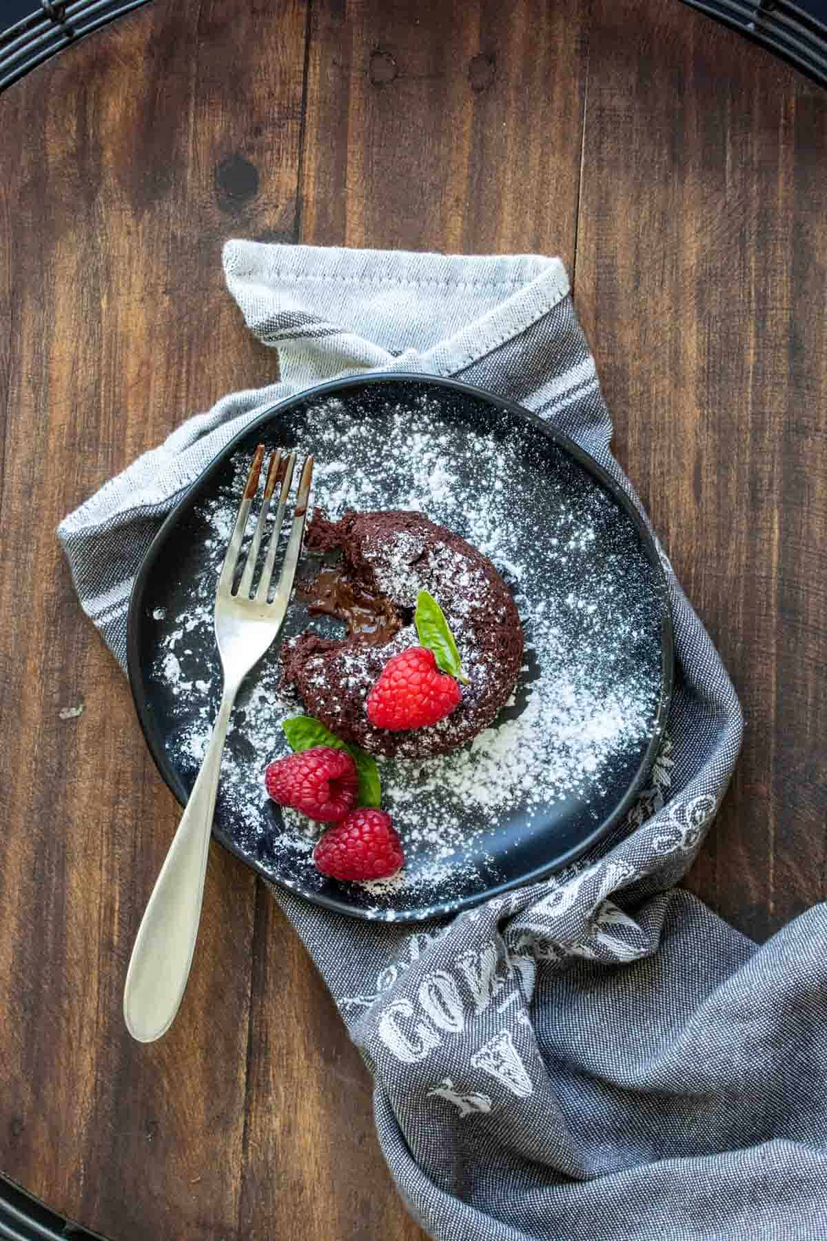 Top view of a chocolate lava cake with a bite out of it on a black plate.