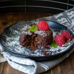 Black plate with a partially eaten chocolate lava cake on it.