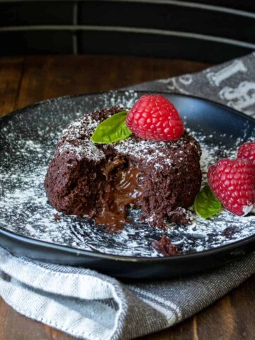 Black plate with a partially eaten chocolate lava cake on it.