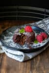 A partially eaten chocolate lava cake with chocolate oozing out the center on a black plate with strawberries.