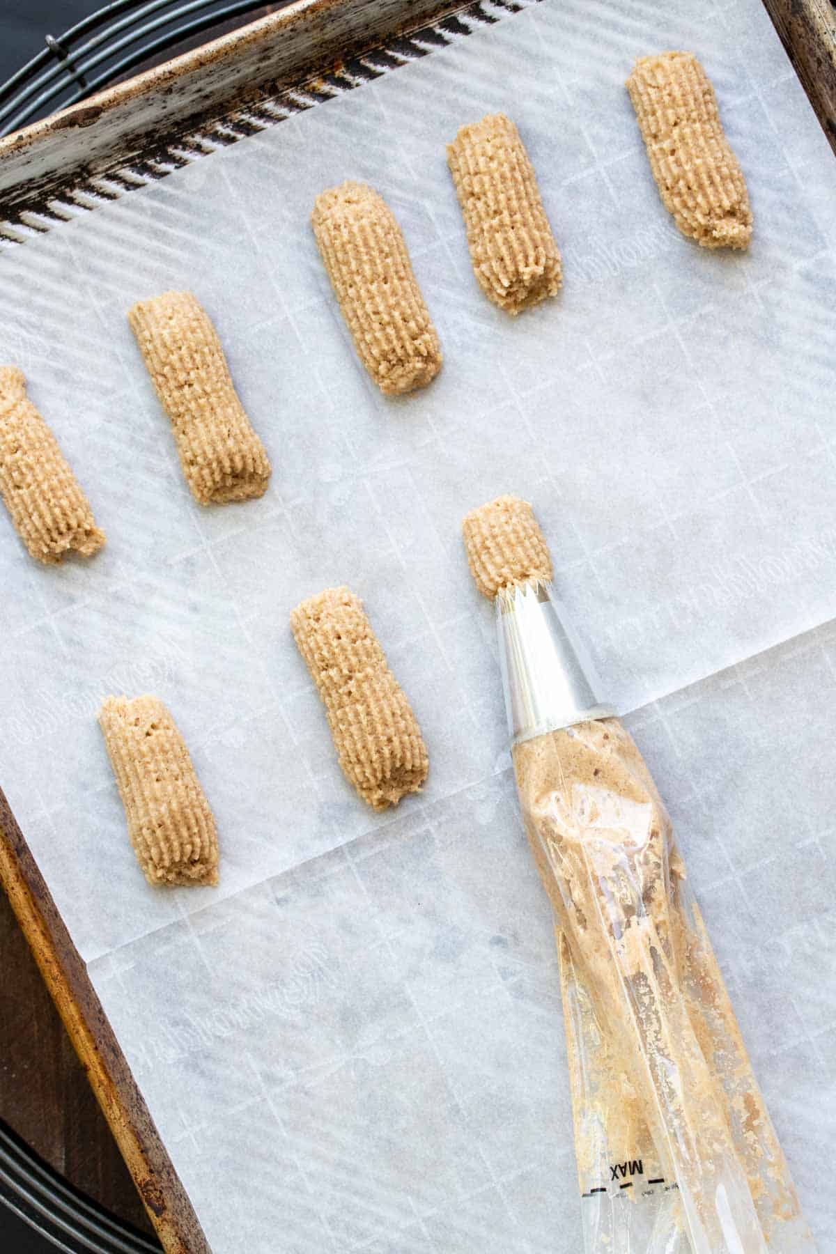 Pastry bag squeezing out batter pieces on a parchment lined baking sheet